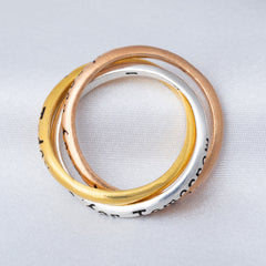 Three stacked rings in gold, rose gold, and silver on a light gray background