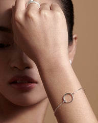 Close-up of a woman's hand wearing a silver bracelet with a circular design on a beige background.