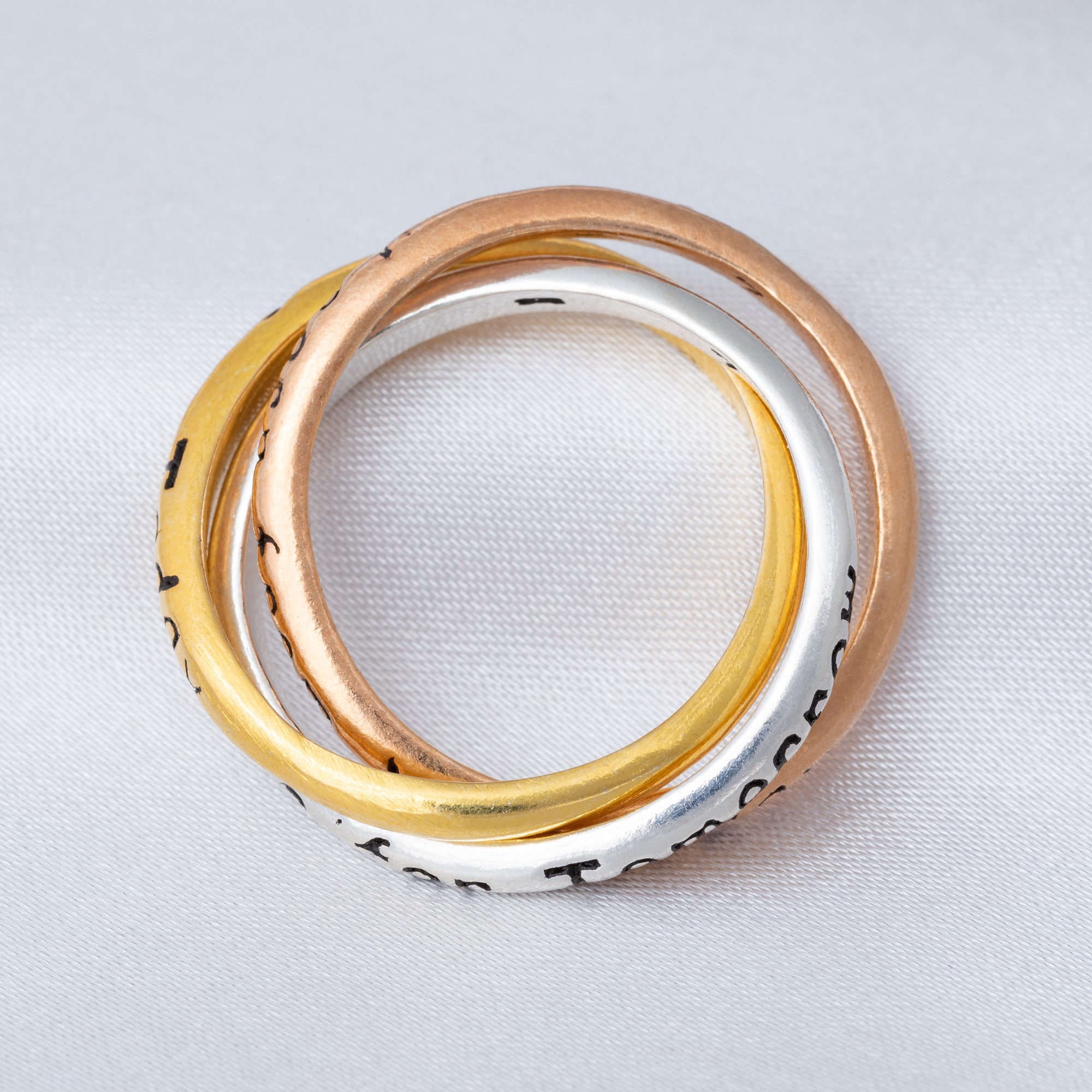 Three stacked rings in gold, rose gold, and silver on a light gray background