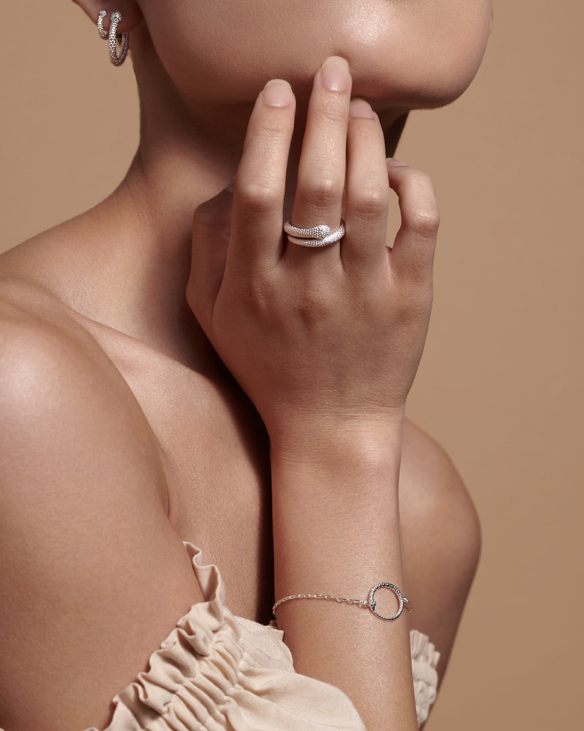 Close-up of a person wearing silver jewelry on a beige background
