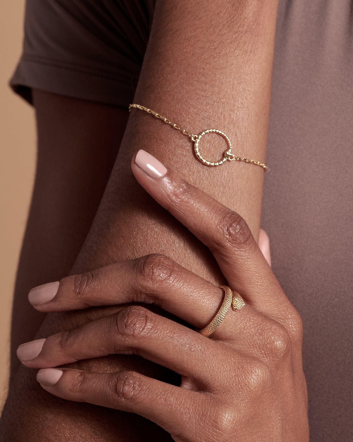 Gold bracelet and ring on a wrist against a brown background