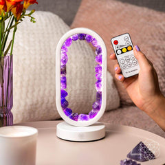 Decorative lamp with purple crystals on a table, held by a hand with a remote control.